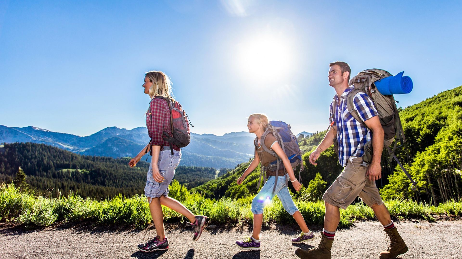 una familia con mochilas camina por un camino hacia las montañas