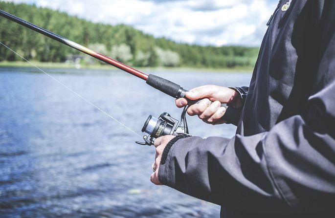 A man holds a fishing rod and a fishing reel on the shore of a lake