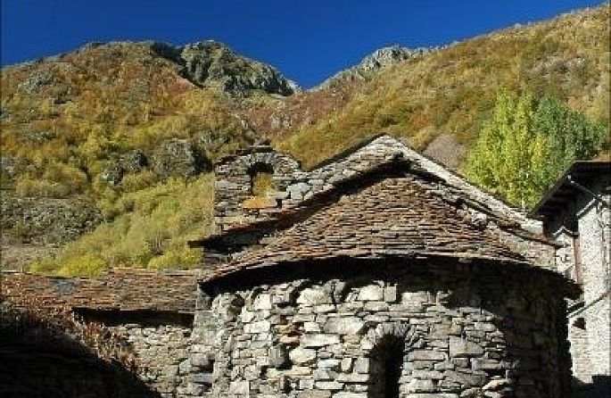 un edifici de pedra amb un sostre de teules i una muntanya al fons.