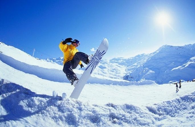 un home en una jaqueta groga salta sobre una taula de surf de neu