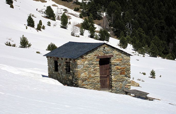 Un petit chalet en pierre se trouve sur une colline enneigée