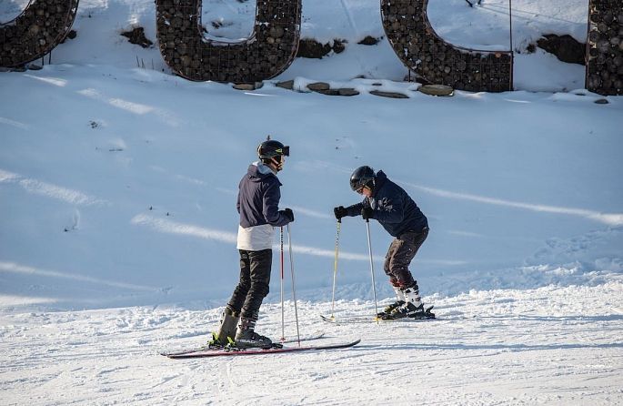 Deux skieurs se tiennent dans la neige devant une grande lettre U