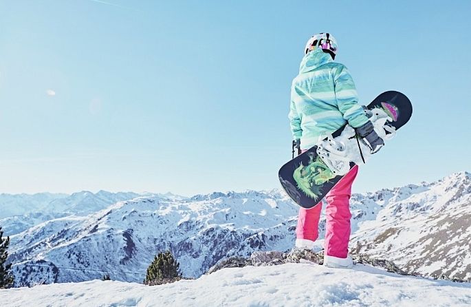 Une femme tient un snowboard au sommet d'une montagne enneigée