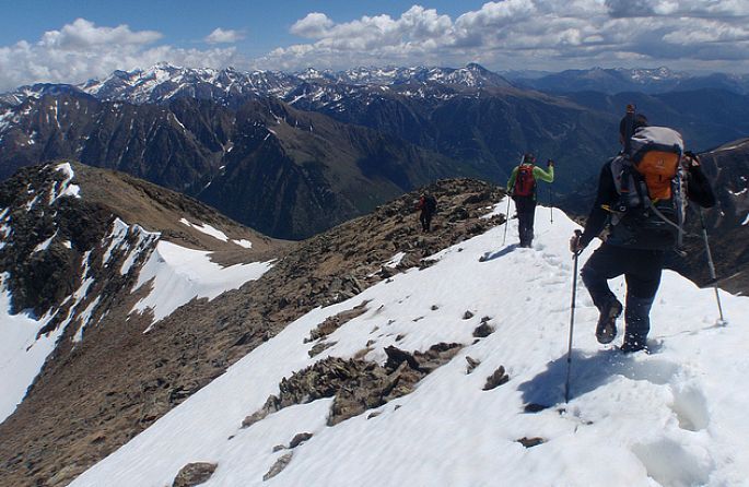 Un homme avec un sac à dos orange escalade une montagne enneigée
