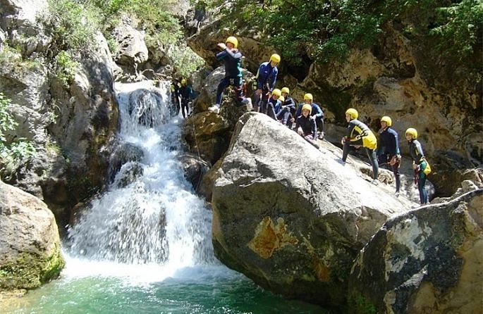 Un groupe de personnes portant des casques jaunes sautent d'un rocher dans une cascade