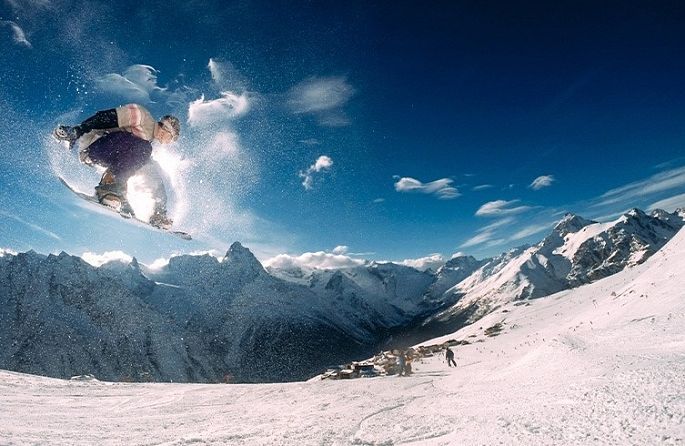 Un snowboarder saute dans les airs devant une montagne enneigée