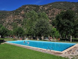 une grande piscine entourée d'herbe et d'arbres avec des montagnes en arrière-plan.